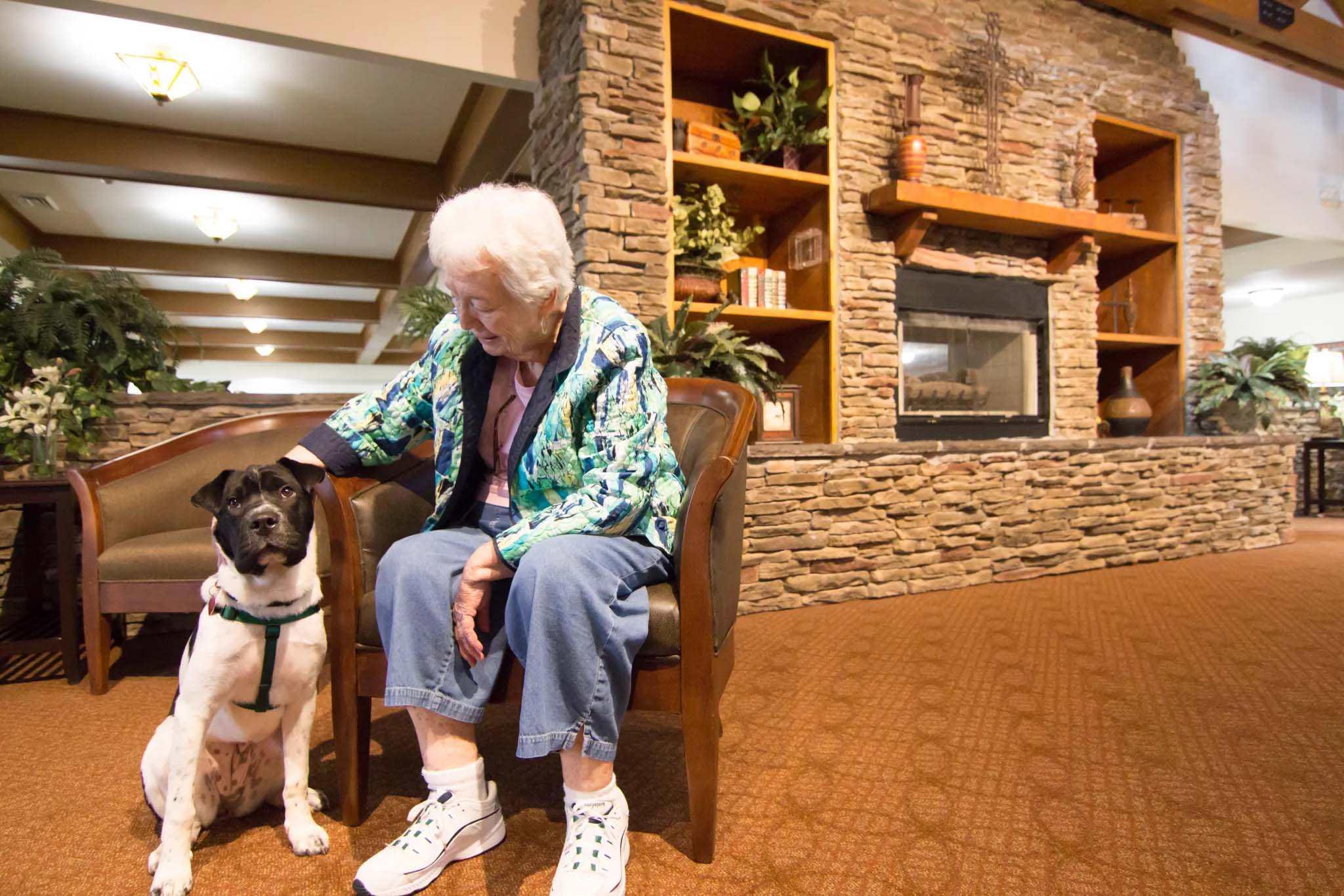 Elderly woman sitting with dog in cozy interior setting.