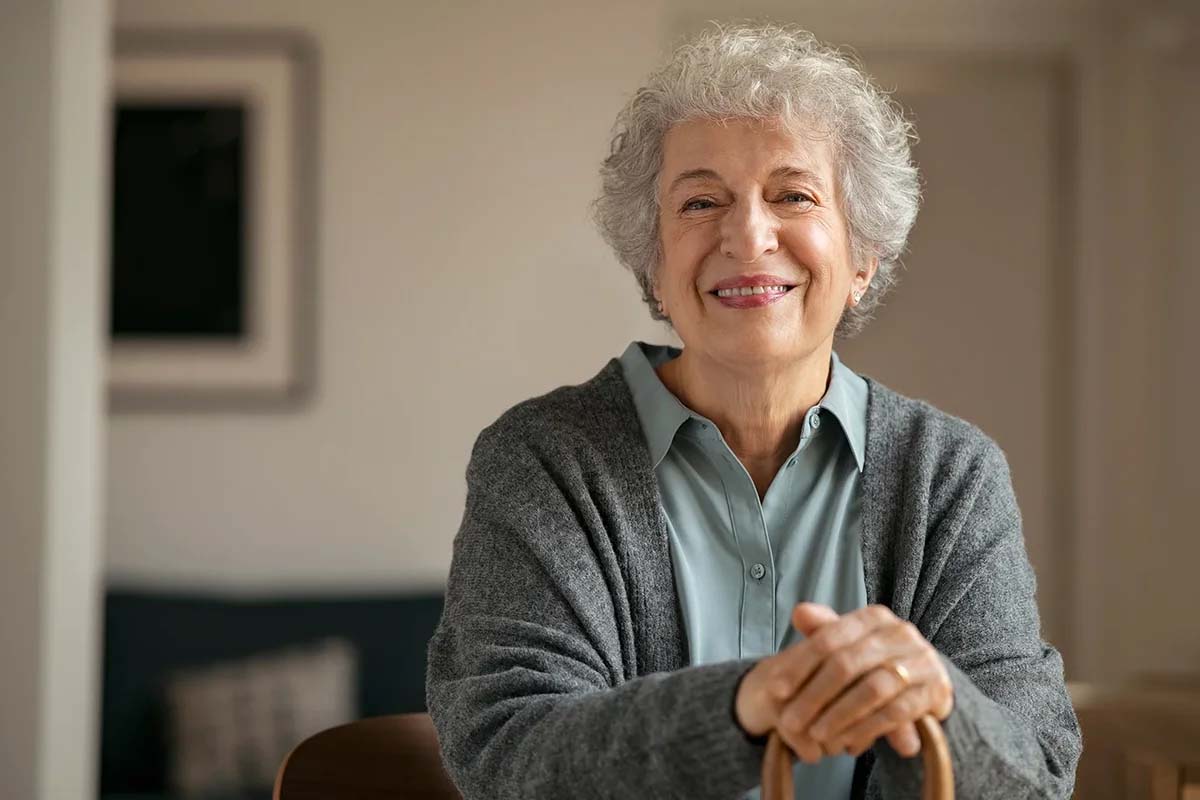 Smiling older woman sitting with a wooden cane.